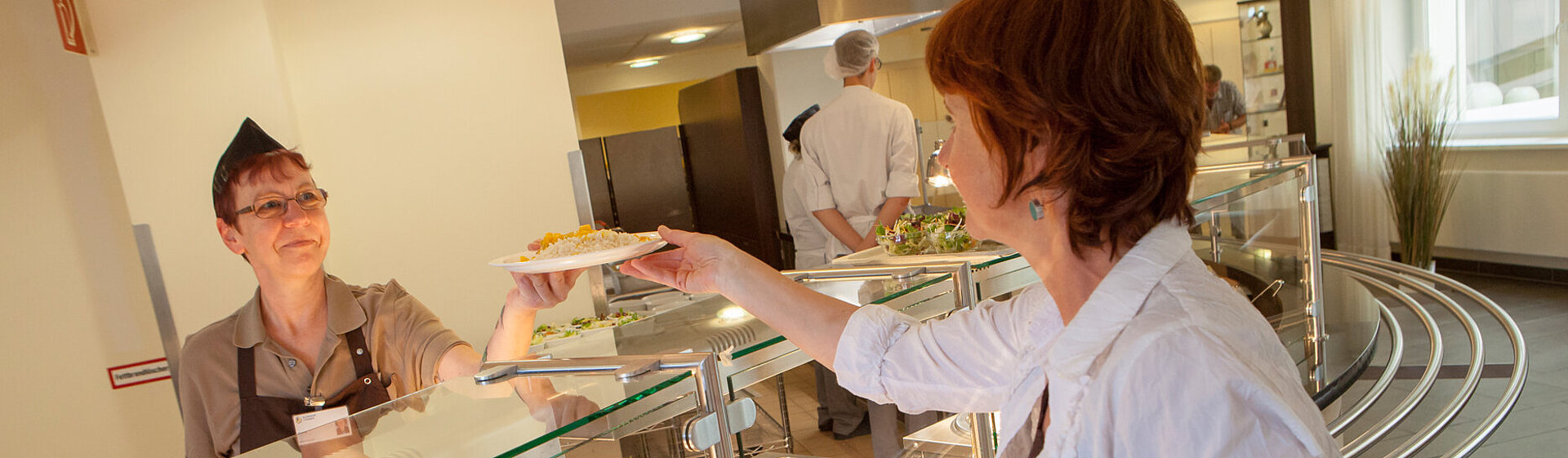Eine Besucherin wird am Tresen der Essensausgabe im Klinik-Restaurant bedient. Eine Besucherin wird am Tresen der Essensausgabe im Klinik-Restaurant bedient.