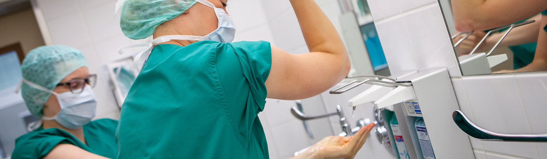 Zwei medizinische Fachkräfte bereiten sich auf eine OP vor und desinfizieren sich Hände und Arme. 