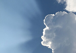 Sonnenstrahlen brechen durch eine Wolke am blauen Himmel