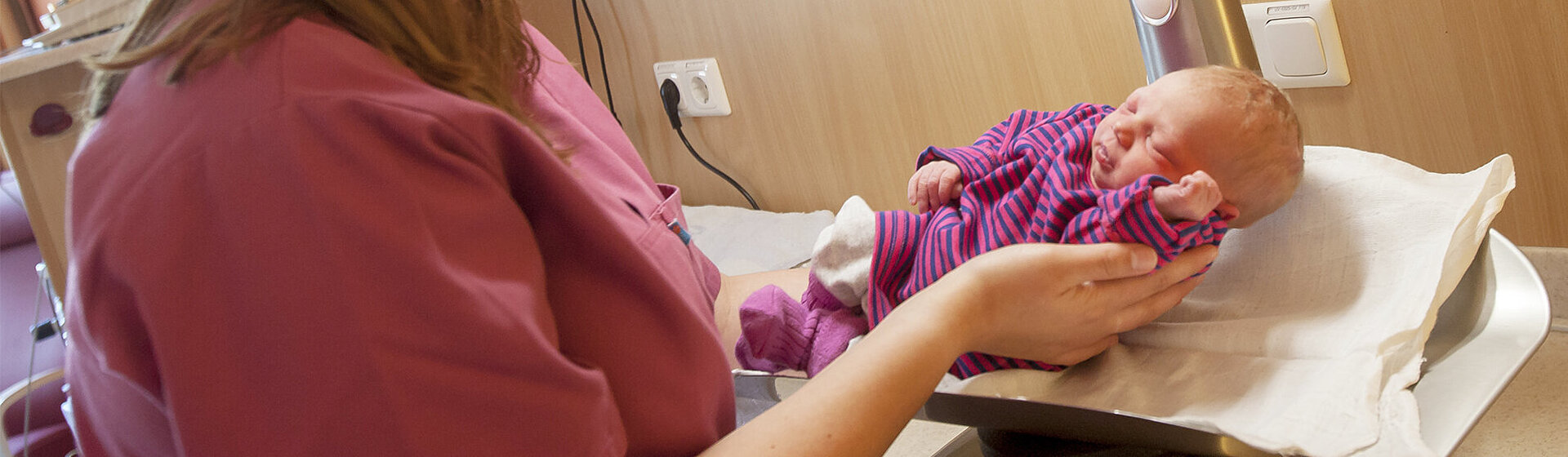 Eine Hebamme legt ein Neugeborenes auf die Waage.