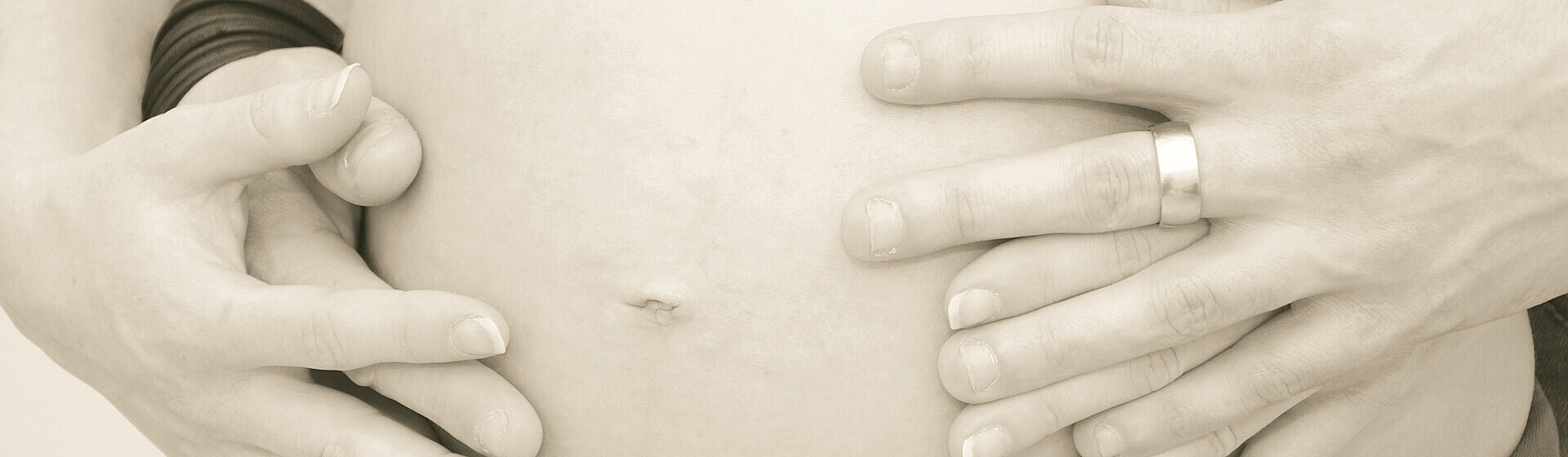 Hände von Mutter und Vater umfassen den Babybauch.