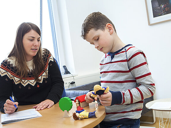 Eine Psychologin unterhält sich mit einem Jungen, der mit Spielzeugfiguren spielt.