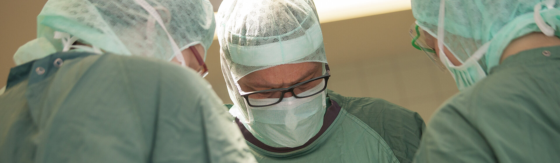 Drei Mediziner in OP-Kleidung stehen am OP-Tisch.