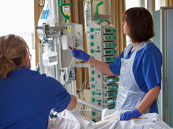 Eine Mitarbeiterin kontrolliert die Überwachungsgeräte, eine Mitarbeiterin kümmert sich um der/dem PatientIn