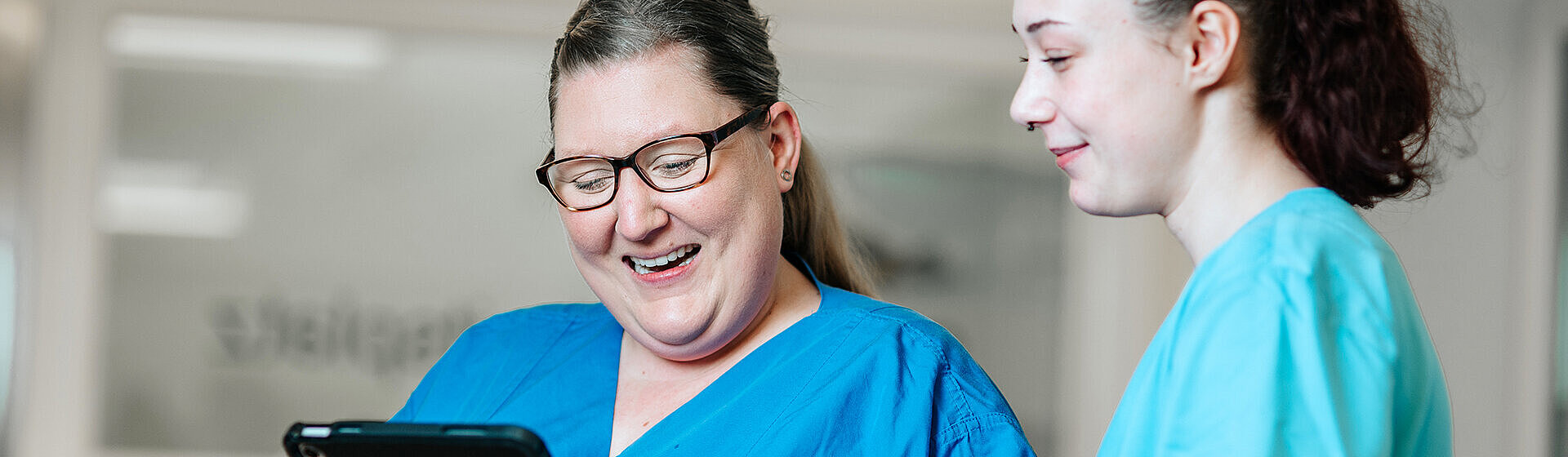 Zwei Pflegefachkräfte schauen lächelnd auf ein Tablett.