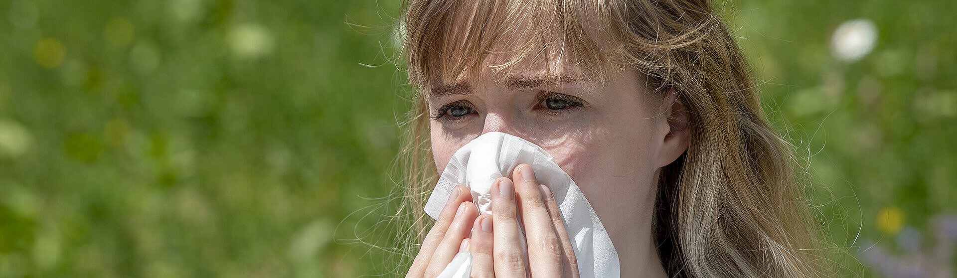 Jugendliche draußen auf einer grünen blühenden Wiese schnäuzt ins Taschentuch.