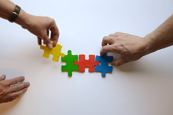 Es sind drei Hände und vier bunte Puzzleteile abgebildet