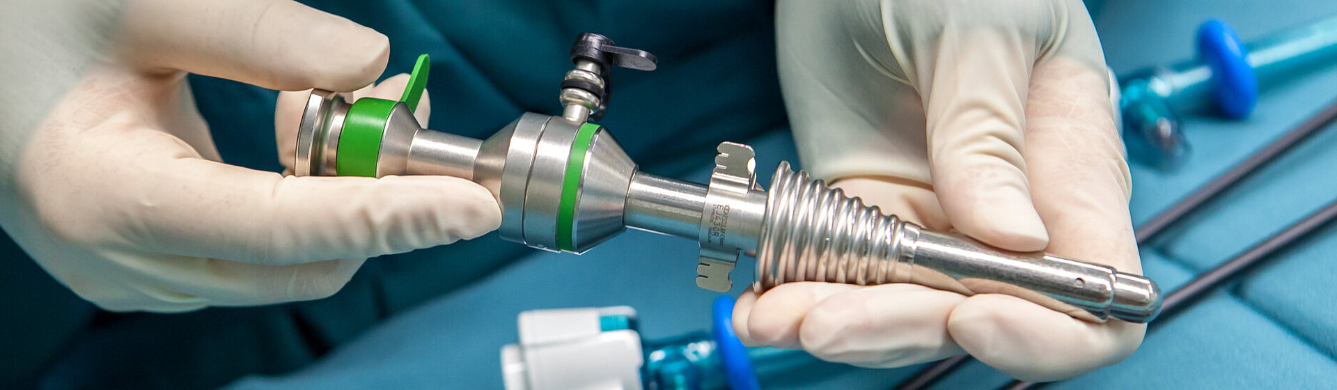 Hände in Latexhandschuhen am OP-Tisch halten ein Trokar (Hülse) für ein Laparoskop für das minimalinvasive Vorgehen bei einer Leistenhernie.