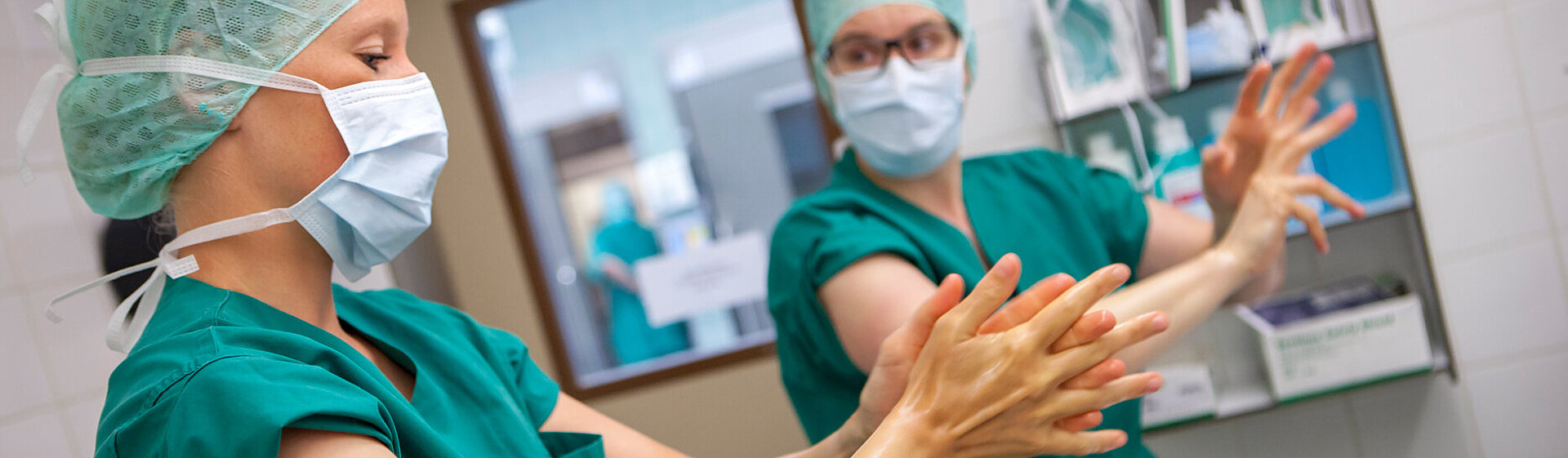 Zwei medizinische OP-Fachkräfte in grüner OP-Kleidung bereiten sich auf eine OP vor und desinfizieren Hände und Arme. Zwei medizinische OP-Fachkräfte in grüner OP-Kleidung bereiten sich auf eine OP vor und desinfizieren Hände und Arme.