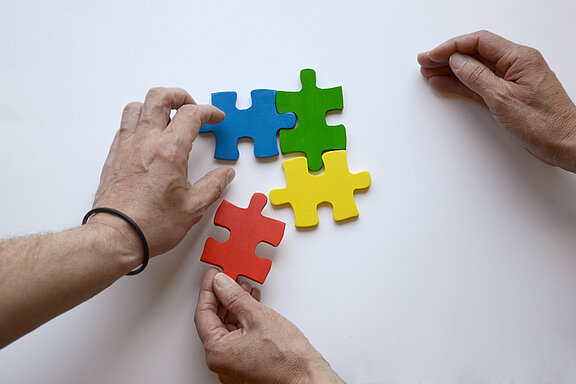 Es sind zwei Hände und vier bunte Puzzleteile abgebildet