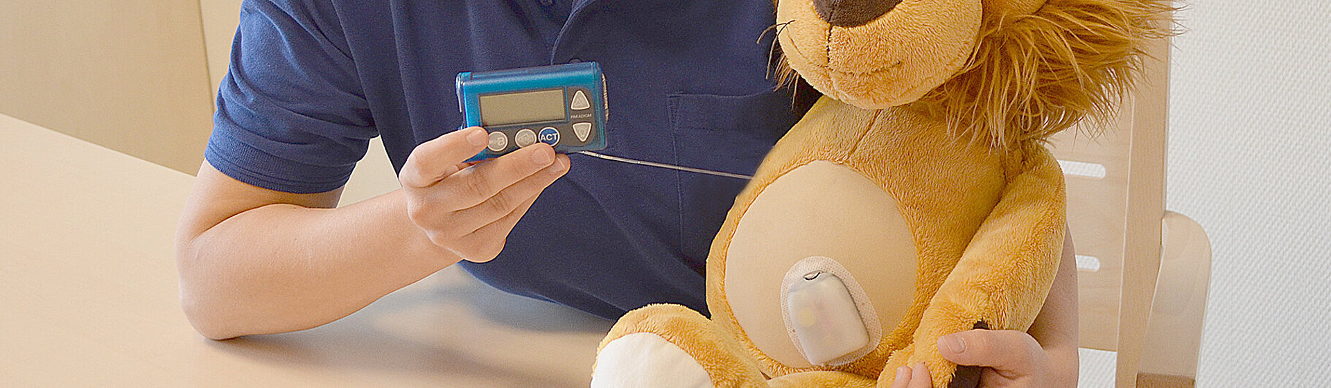 Oberärztin Nadine Scheffler hält ein Blutzuckermessgerät in der Hand, neben ihr am Tisch sitzt ein Kuscheltier (Löwe).