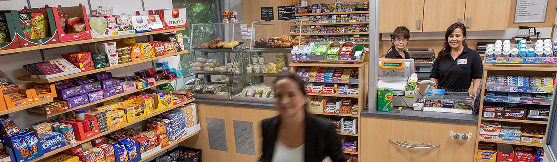 Eine Besucherin hat im Kiosk eingekauft, hinterm Tresen stehen zwei Mitarbeitende. Eine Besucherin hat im Kiosk eingekauft, hinterm Tresen stehen zwei Mitarbeitende.