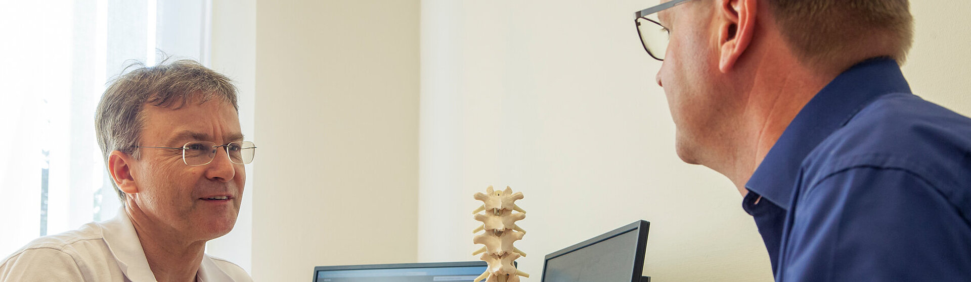 Dr. med. Wolfram Kluge klärt einen Patienten anhand eines Wirbelsäulenmodells über die SCS-Rückenmarkstimulation. auf. Dr. med. Wolfram Kluge klärt einen Patienten anhand eines Wirbelsäulenmodells über die SCS-Rückenmarkstimulation. auf.