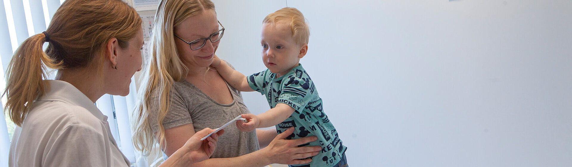 Kinderärztin unterhält sich mit einer Mutter und Ihrem Kind im Untersuchungszimmer.