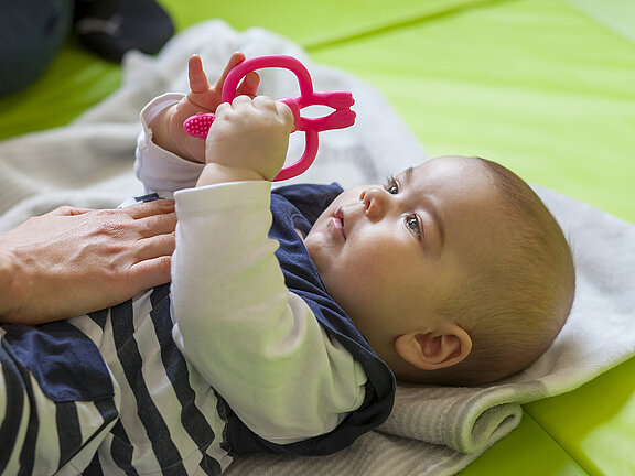 Ein Baby liegt auf einer Decke und spielt.