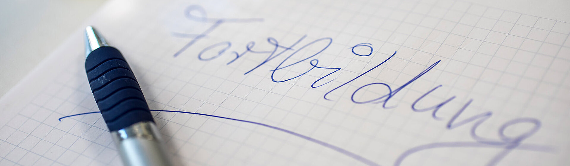 Auf einem Blatt Papier steht das Wort Fortbildung, darauf liegt ein Kugelschreiber.