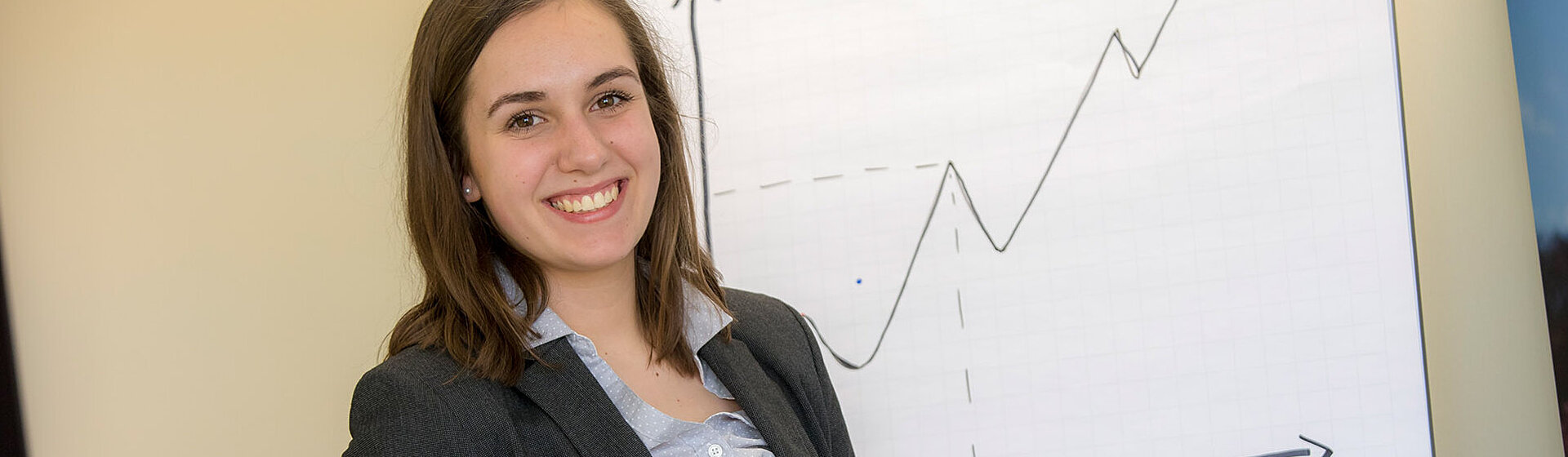 Eine Mitarbeiterin hält lächelnd einen Stift in der Hand - im Hintergrund steht ein Flipchart.