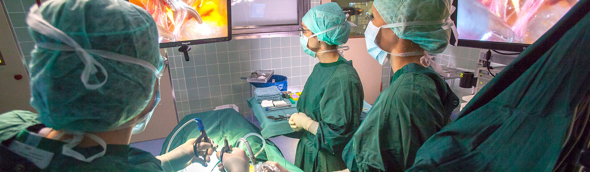 Operationssituation eines Minimal-invasiven Eingriffs, Operateur und med. Fachkräfte blicken auf den OP-Monitor.